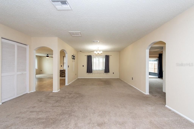 empty room featuring a healthy amount of sunlight, a textured ceiling, and ceiling fan with notable chandelier