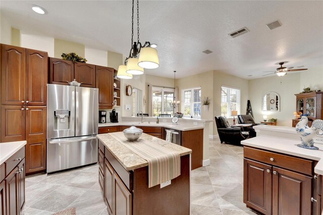 kitchen with a textured ceiling, stainless steel appliances, ceiling fan, pendant lighting, and a center island