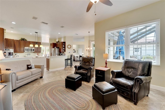 tiled living room featuring a healthy amount of sunlight and ceiling fan with notable chandelier