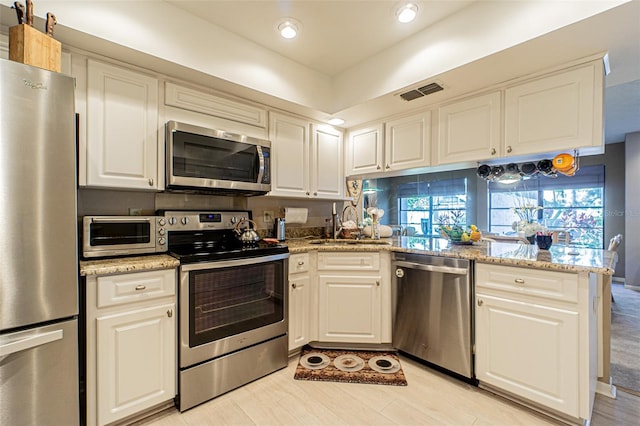 kitchen with white cabinetry, stainless steel appliances, and light stone counters