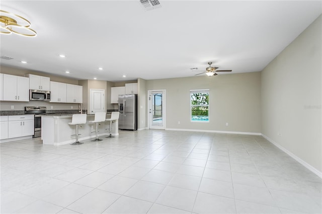 kitchen with a kitchen bar, ceiling fan, appliances with stainless steel finishes, a kitchen island, and white cabinets