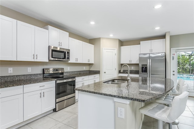 kitchen featuring dark stone countertops, sink, white cabinetry, a kitchen island with sink, and appliances with stainless steel finishes