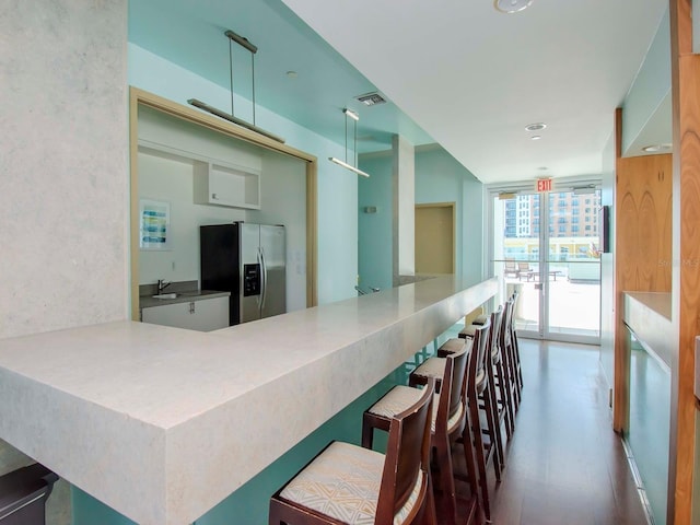 kitchen with dark hardwood / wood-style floors, stainless steel fridge, a kitchen breakfast bar, expansive windows, and kitchen peninsula