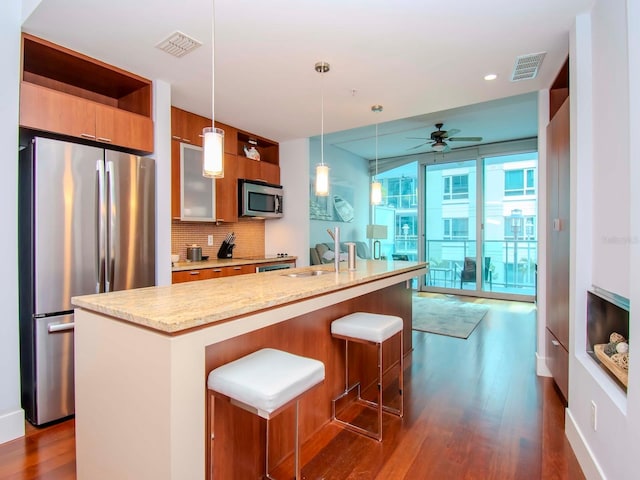 kitchen featuring a breakfast bar area, stainless steel appliances, light stone counters, tasteful backsplash, and decorative light fixtures