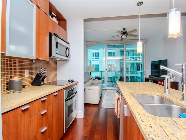 kitchen with sink, backsplash, stainless steel appliances, light stone countertops, and decorative light fixtures