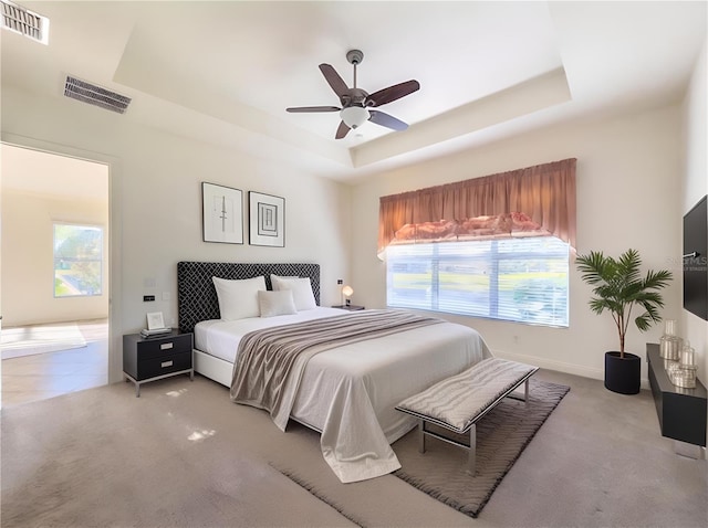 carpeted bedroom featuring a raised ceiling, multiple windows, and ceiling fan