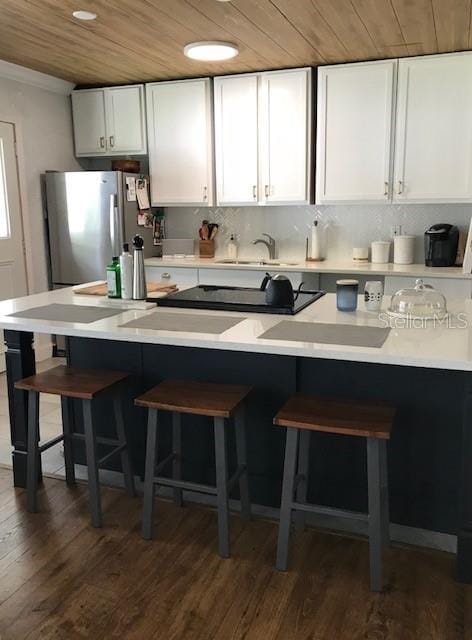 kitchen featuring white cabinets, wood ceiling, stainless steel fridge, dark wood-type flooring, and a kitchen bar