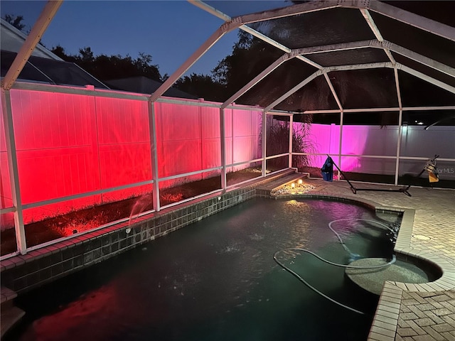 pool at twilight featuring glass enclosure and a patio area