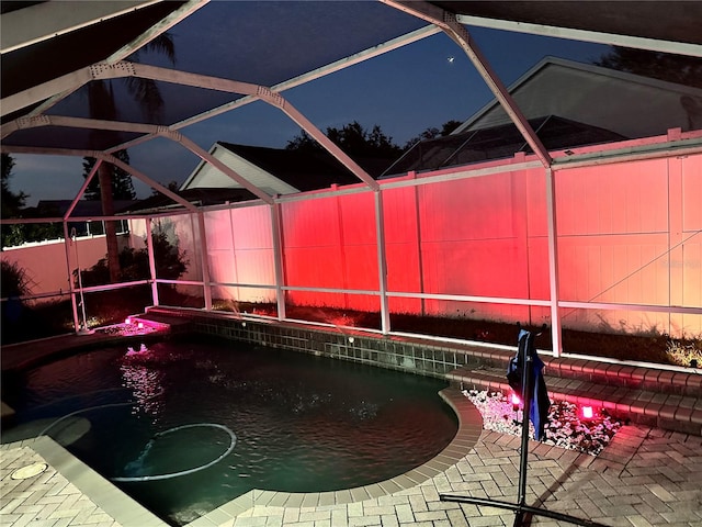 pool at twilight with glass enclosure and a patio