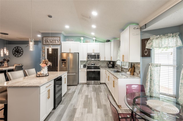 kitchen with appliances with stainless steel finishes, lofted ceiling, sink, and hanging light fixtures