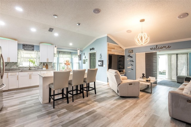 living room featuring light wood-type flooring, lofted ceiling, plenty of natural light, and a textured ceiling