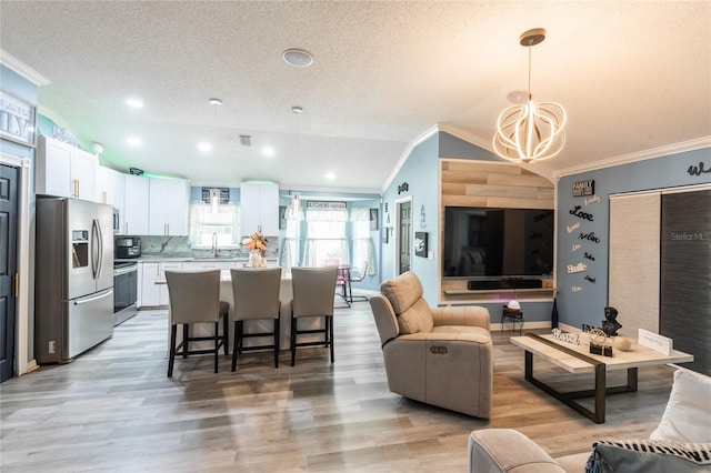 living room featuring a textured ceiling, crown molding, sink, lofted ceiling, and light wood-type flooring