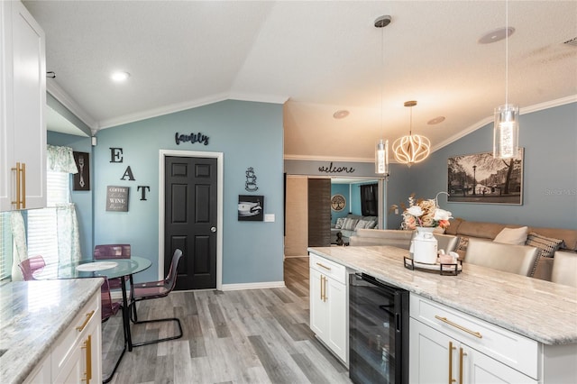 kitchen featuring light hardwood / wood-style flooring, beverage cooler, hanging light fixtures, vaulted ceiling, and white cabinets