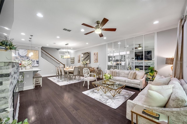 living room with ceiling fan with notable chandelier, a fireplace, dark hardwood / wood-style floors, and ornamental molding