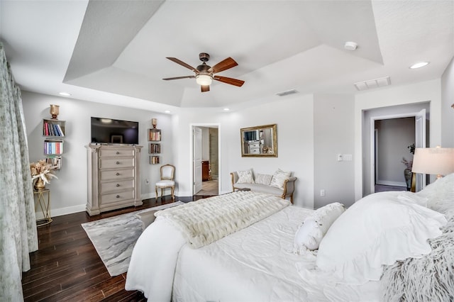 bedroom featuring a raised ceiling, ceiling fan, dark hardwood / wood-style floors, and connected bathroom