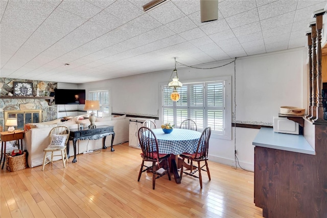 dining room featuring light wood-type flooring, a healthy amount of sunlight, and a stone fireplace