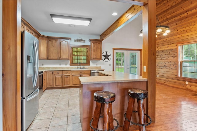 kitchen with wood walls, sink, light hardwood / wood-style flooring, stainless steel appliances, and a breakfast bar