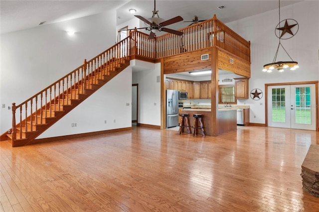 unfurnished living room with light hardwood / wood-style floors, ceiling fan, and high vaulted ceiling