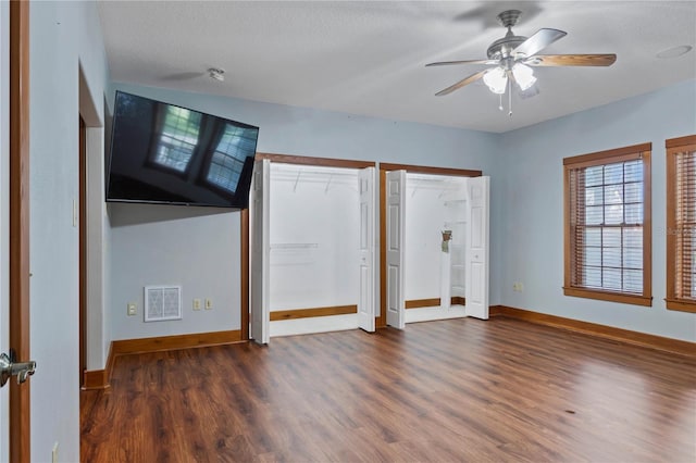 unfurnished bedroom featuring two closets, ceiling fan, dark wood-type flooring, and a textured ceiling