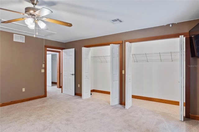 unfurnished bedroom with ceiling fan, two closets, and light carpet