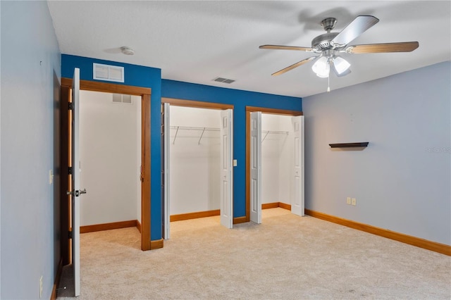 unfurnished bedroom with light carpet, ceiling fan, and multiple closets