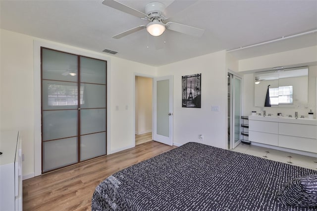 bedroom with light wood-type flooring, ceiling fan, and connected bathroom