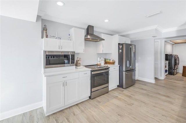 kitchen with appliances with stainless steel finishes, light hardwood / wood-style floors, white cabinetry, washer and dryer, and wall chimney exhaust hood