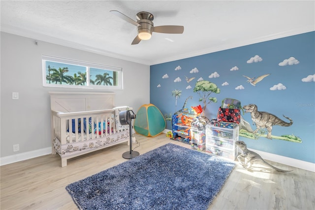 bedroom featuring crown molding, ceiling fan, wood-type flooring, and a crib