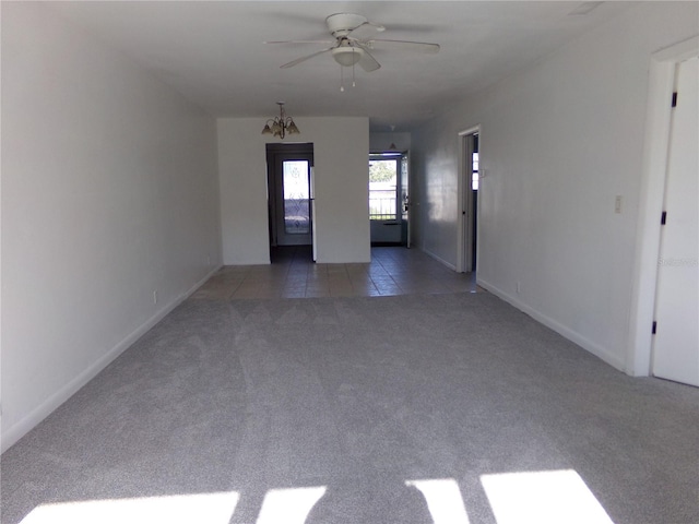 carpeted spare room featuring ceiling fan with notable chandelier