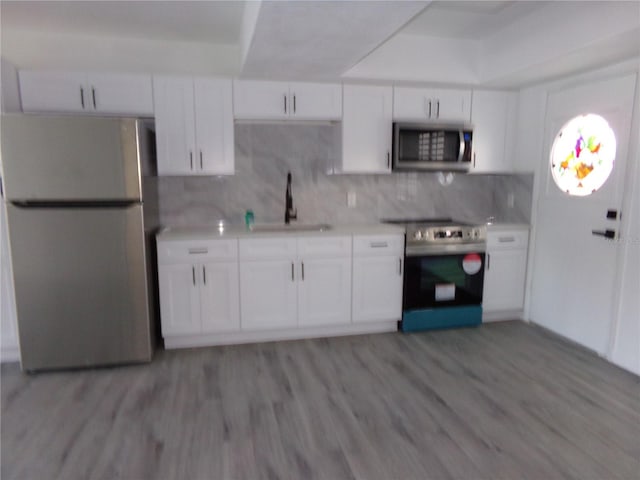 kitchen with light wood-type flooring, white cabinetry, tasteful backsplash, sink, and appliances with stainless steel finishes