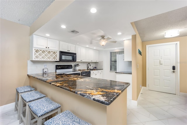 kitchen featuring white cabinets, electric range oven, kitchen peninsula, and a breakfast bar area