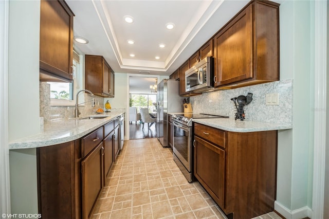 kitchen featuring light wood-type flooring, appliances with stainless steel finishes, backsplash, and a raised ceiling