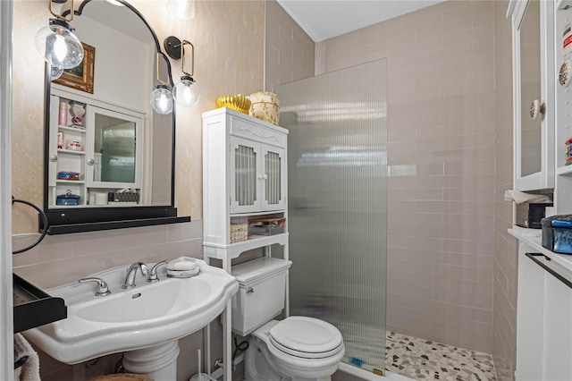 bathroom with tiled shower, toilet, sink, and tasteful backsplash