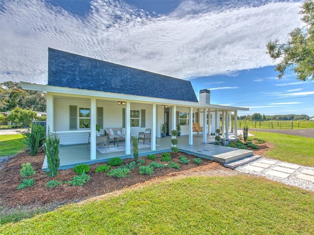view of front of home with a front lawn, a chimney, a shingled roof, and covered porch