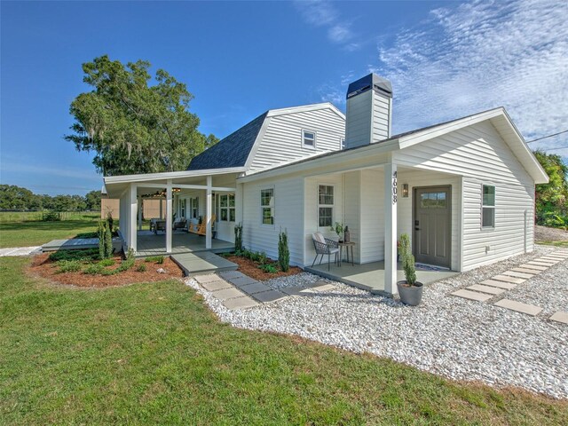 back of house with a lawn, a chimney, a gambrel roof, and a patio area