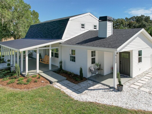 back of property with a gambrel roof, a chimney, a patio area, and roof with shingles