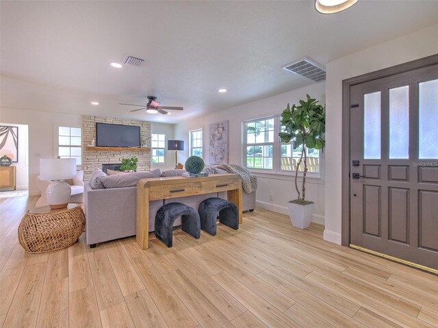 living room with light wood-type flooring, ceiling fan, and a fireplace