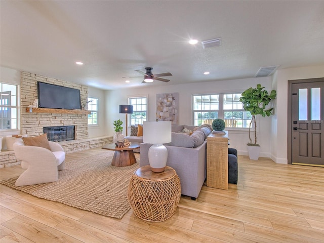 living room featuring light hardwood / wood-style flooring, ceiling fan, a wealth of natural light, and a stone fireplace