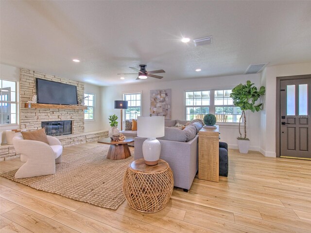 living area featuring a fireplace, visible vents, light wood-style floors, and a ceiling fan