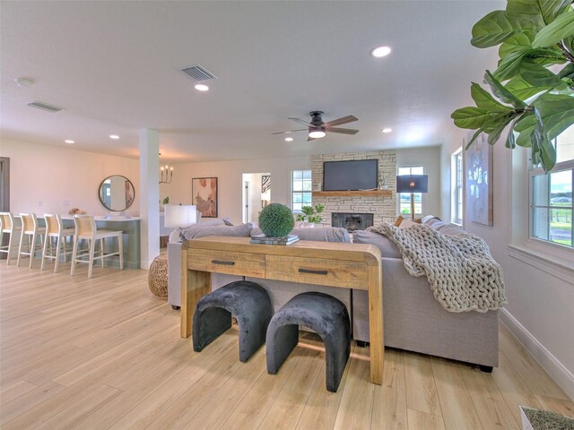 living area featuring a fireplace, visible vents, a ceiling fan, and wood finished floors