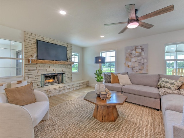 living room with light hardwood / wood-style floors, ceiling fan, and a stone fireplace