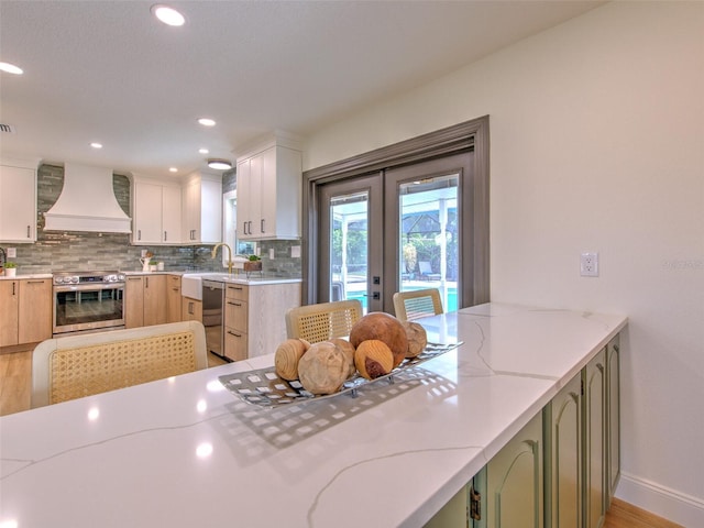 kitchen featuring french doors, appliances with stainless steel finishes, custom range hood, white cabinets, and light hardwood / wood-style floors