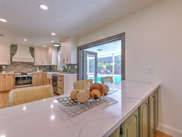 kitchen featuring light stone counters, backsplash, stainless steel electric range, light wood-type flooring, and custom exhaust hood