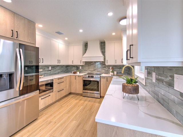 kitchen with light brown cabinetry, premium range hood, appliances with stainless steel finishes, light hardwood / wood-style floors, and sink