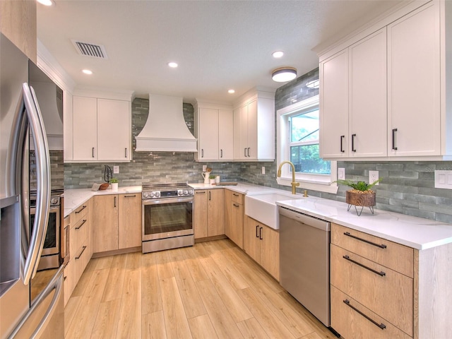 kitchen featuring backsplash, light wood-type flooring, appliances with stainless steel finishes, custom exhaust hood, and sink