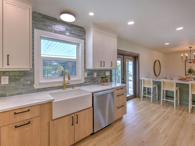 kitchen featuring light stone counters, a sink, light wood finished floors, stainless steel dishwasher, and decorative backsplash