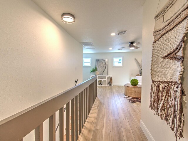 hall with light wood-style flooring, an upstairs landing, baseboards, and visible vents