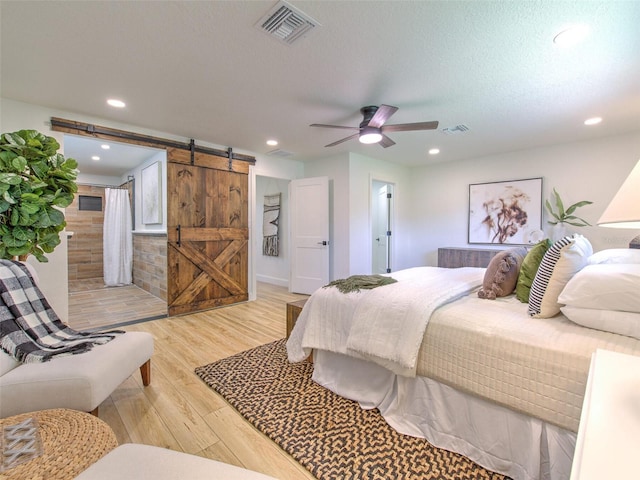 bedroom with a barn door, ceiling fan, a textured ceiling, and light hardwood / wood-style flooring