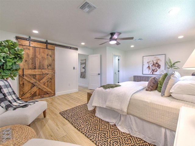 bedroom featuring a barn door, ceiling fan, a textured ceiling, and light hardwood / wood-style flooring