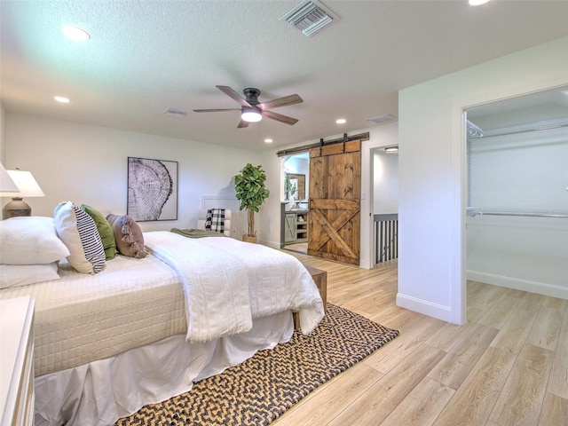 bedroom featuring a walk in closet, light hardwood / wood-style flooring, a closet, a barn door, and ceiling fan